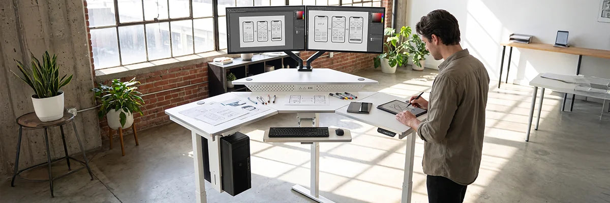 Creative professional sketching on VersaDesk electric drafting table with dual monitors in bright modern studio workspace