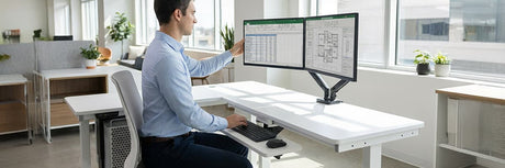 Man adjusting a dual-monitor ergonomic arm mounted on a height-adjustable standing desk