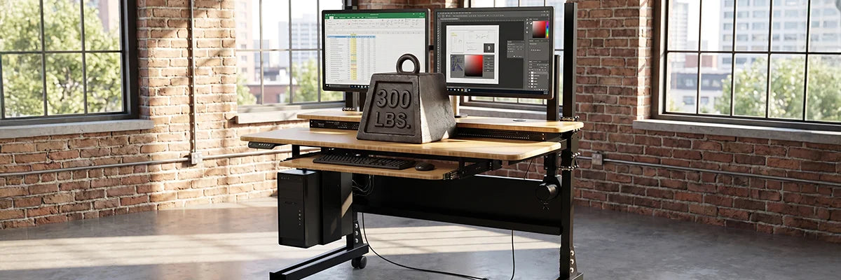 VersaDesk Foundry Bench standing desk supporting 300 LBS weight with dual monitors in industrial brick wall office setting