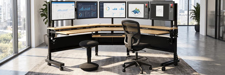 VersaDesk Foundry Bench U-shaped standing desk with five monitors, ergonomic mesh chair and black wobble stool in bright executive office with city view