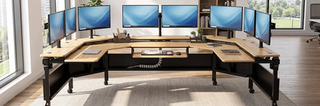 VersaDesk Foundry Bench wraparound bamboo standing desk with eight curved monitors, keyboard tray and office accessories in bright modern office with large windows