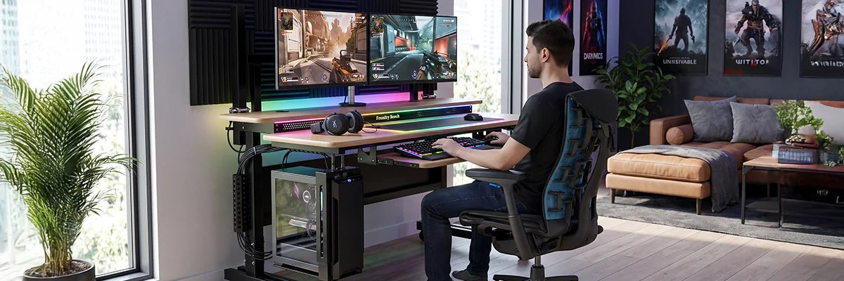 Gamer sitting at a VersaDesk electric standing desk with dual gaming monitors, RGB lighting, gaming chair, and PC tower in a stylish gaming room with posters, showcasing the ultimate gaming setup.