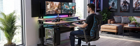 Gamer sitting at a VersaDesk electric standing desk with dual gaming monitors, RGB lighting, gaming chair, and PC tower in a stylish gaming room with posters, showcasing the ultimate gaming setup.