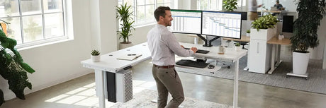 Woman standing at a height-adjustable desk with dual monitors, illustrating a customized standing desk routine