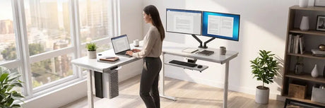Woman working at an L-shaped standing desk with laptop on the main run and a dual-monitor arm mounted on the corner return