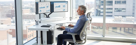 Professional man sitting at an adjustable height desk with proper ergonomic office chair and dual monitors, showing the sitting position of a sit-stand desk solution.