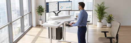 Man working at a white standing desk with dual monitors and an integrated cable management tray system, demonstrating clutter-free cable routing and CPU holder setup in a modern bright office.