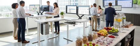 Modern office with employees working at standing desks alongside a healthy snack bar featuring fresh fruits, nuts, and yogurt, promoting workplace wellness and employee satisfaction.