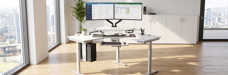Clean white ergonomic standing desk with dual monitors, organized cable management, and CPU holder in a minimalist modern office with city views, demonstrating a clutter-free workspace organization system.