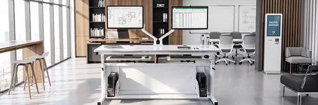 Modern specialty workspace with height-adjustable computer desks, dual monitors on white mounting stands, classroom chairs, whiteboard, and a digital signage kiosk near floor-to-ceiling windows