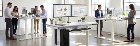Multiple office workers collaborating and working at electric standing desks in a bright open-plan office, showing how standing desks benefit teams and improve workplace health.