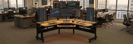 Professional trading floor with a curved multi-monitor workstation displaying stock charts and financial data on multiple screens mounted on monitor arms, showcasing an ergonomic trading desk setup in a corporate office.