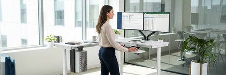 Man standing at a dual-monitor height-adjustable desk in a bright office, representing common standing desk health claims