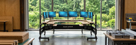 VersaDesk curved multi-monitor standing desk with bamboo surface in a sustainable manufacturing workshop surrounded by greenery, showcasing eco-friendly workspace furniture production.