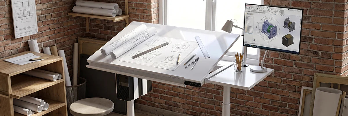 White VersaDesk corner drafting table with tilted surface holding architectural blueprints, pencils and ruler, CAD monitor on arm mount in small brick studio with rolled drawings and wooden shelves