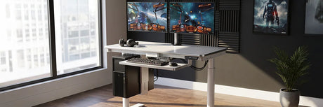 White VersaDesk gaming standing desk with dual curved monitors showing space game, headphones and CPU mount in room with acoustic foam panels