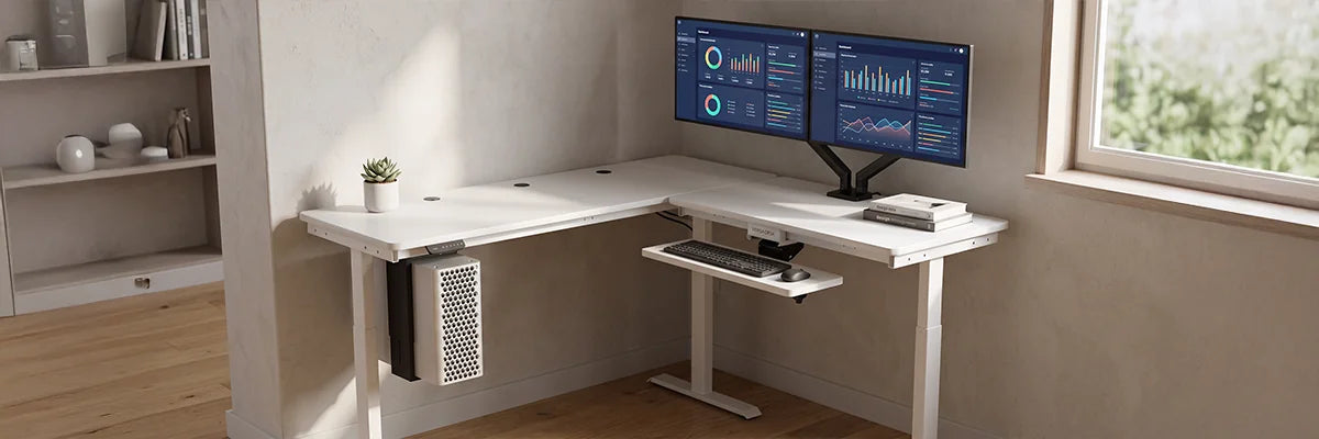 White VersaDesk L-shaped standing desk with dual analytics monitors in compact corner home office with natural light and minimal decor