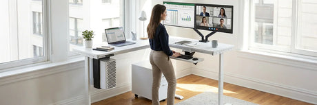 Woman using a white standing desk with an under-desk storage drawer unit on casters and side-mounted CPU holder, showcasing organized workspace accessories and add-on storage in a bright home office.