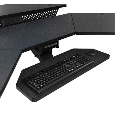 Close-up of the VersaDesk PowerLift CSD standing desk converter in black, showing the pull-out keyboard and mouse tray with a built-in power outlet strip